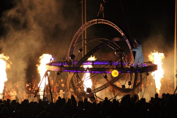 effet de scène flammes Un spectacle nocturne avec des flammes, une structure en mouvement et une foule émerveillée.