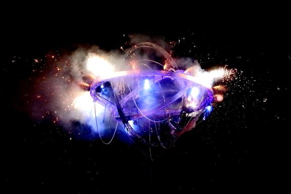 Final pyrotechnique Un véhicule futuriste avec des lumières et des effets pyrotechniques sur fond noir.