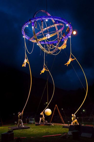 corde lisse Performers manipulate a large, illuminated structure with suspended elements in a dark sky.
