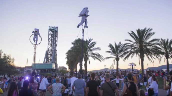 artistes de rue Foule animée sous un ciel crépusculaire, avec des sculptures d'astronautes et des palmiers.