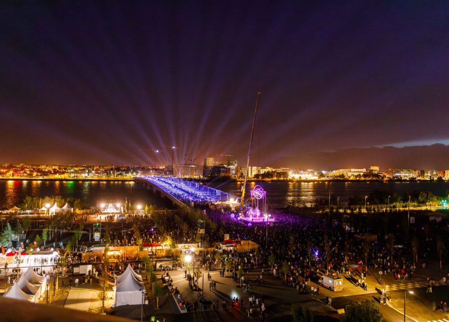 inauguration Pont Simone Veil Bordeaux Vue nocturne d'une ville illuminée avec des rayons de lumière et un pont en arrière-plan.
