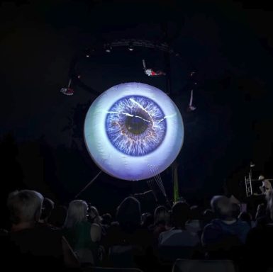 spectacle oeil geant Un œil géant lumineux suspendu, entouré de spectateurs émerveillés.