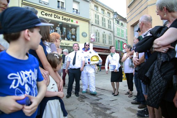 spectacle déambulation allégorie de la grenouille Groupe de personnes rassemblées autour d'un personnage déguisé en marin dans une rue animée.