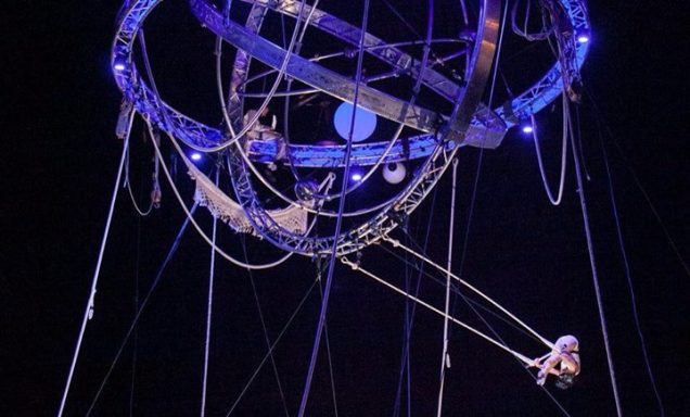 numéro trapèze ballant Un artiste de cirque suspendu à une structure en métal, entouré de lumière.