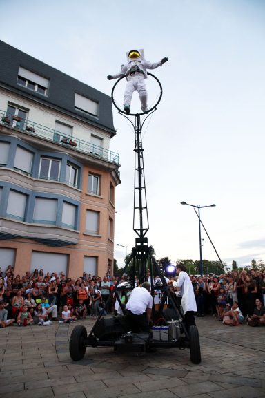 spectacle de rue allégorie de la grenouille Un artiste de cirque effectue un numéro en hauteur sur un monocycle, devant une foule.