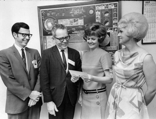 en scène pour la parade Quatre personnes souriantes, discutant autour d'un document, dans un cadre formel.