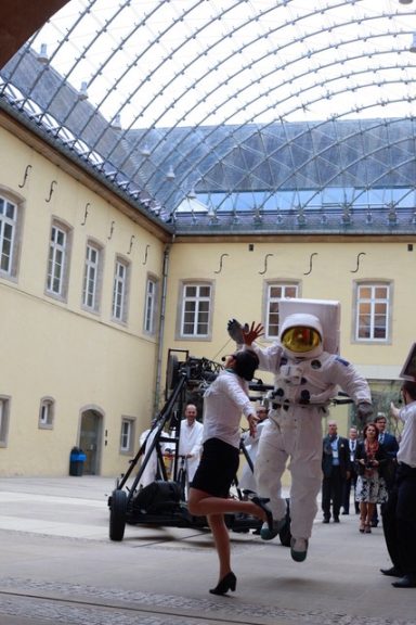 parade de rue Une femme en jupe danse avec un astronaute dans un grand hall sous une verrière.