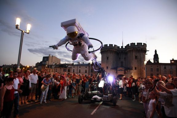 spectacle déambulation allégorie de la grenouille Un astronaute volant au-dessus d'une foule devant un château au crépuscule.