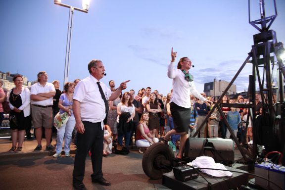 spectacle déambulation allégorie de la grenouille Une foule attentive assiste à un spectacle en plein air, avec un artiste sur scène.