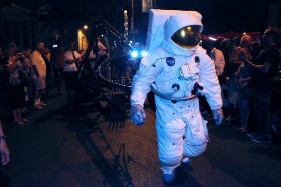 déambulation theâtrale Un astronaute en combinaison marche parmi une foule lors d'un événement nocturne.