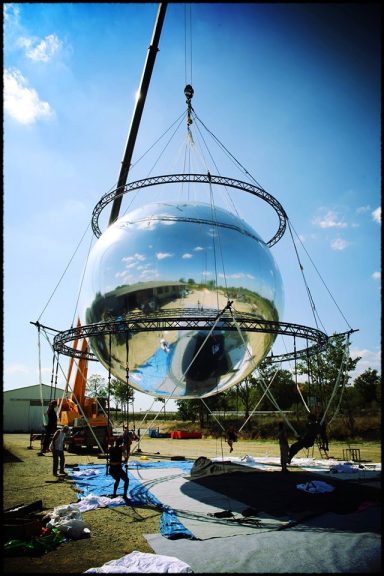 décor de spectacle mirroir Installation d'une grande sphère réfléchissante avec des ouvriers et une grue.