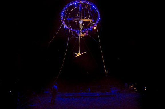 spectacle de rue galileo Artiste acrobatique suspendu dans les airs, éclairé par des lumières colorées.