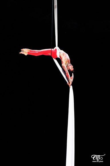 aerial silk Artiste de cirque en apesanteur, suspendu à un tissu, en tenue rouge sur fond noir.