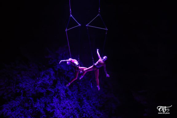 spectacle aérien lumineux Deux artistes suspendus en hauteur, effet dramatique de lumière violette en arrière-plan.