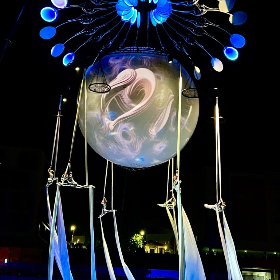 spectacle LE Grand Mire Une scène artistique nocturne avec une grande sphère suspendue et des éléments aériens.