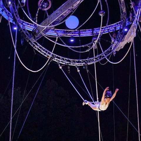 acrobate trapèze Artiste de cirque en suspension, exécutant des figures acrobatiques sous des lumières violettes.