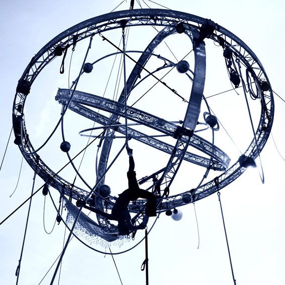 acrobate corde lisse Artiste acrobatique suspendu dans une structure en forme de sphère, ciel en arrière-plan.